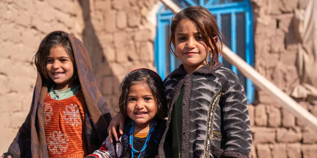 Afghani girls Malayeka and her sister Maryam stand in front of their mud brick home