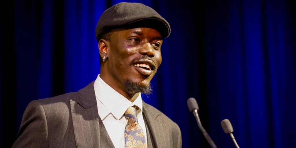 Abraham Kuol stands on a stage and is talking into a microphone